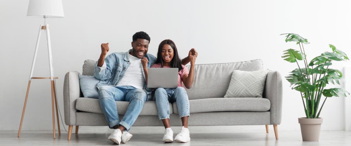 Couple sitting on couch looking at laptop and celebrating