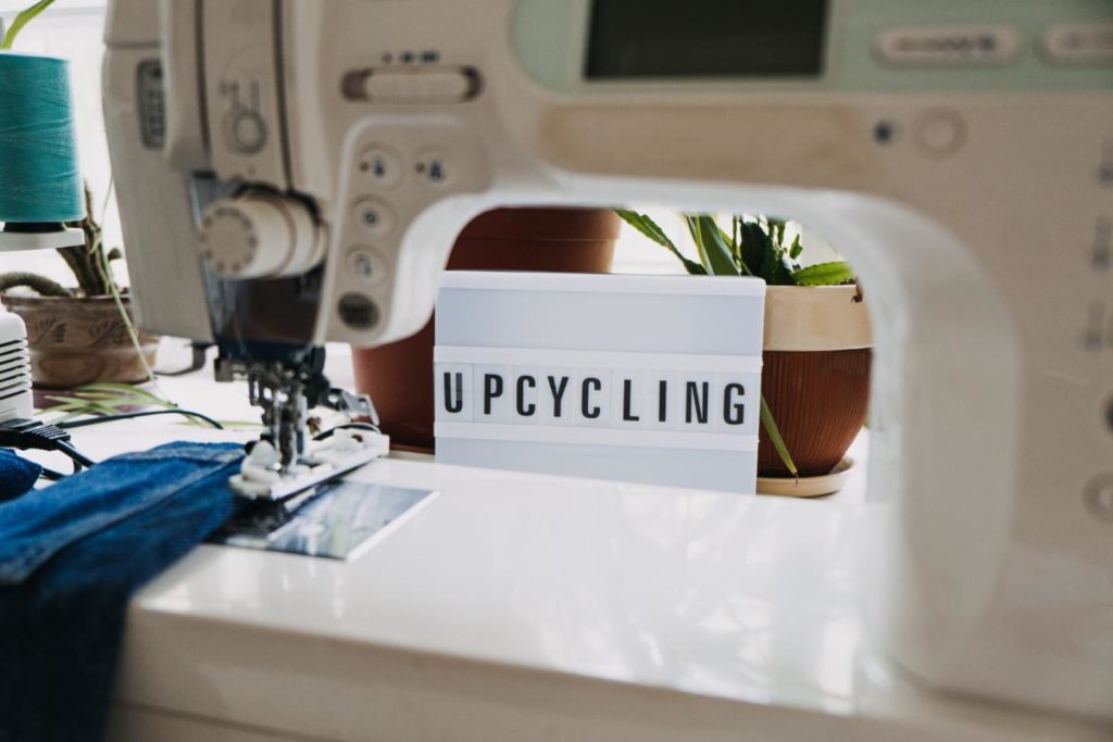 upcycling text on a light board behind a sewing machines with old blue jeans in the background.