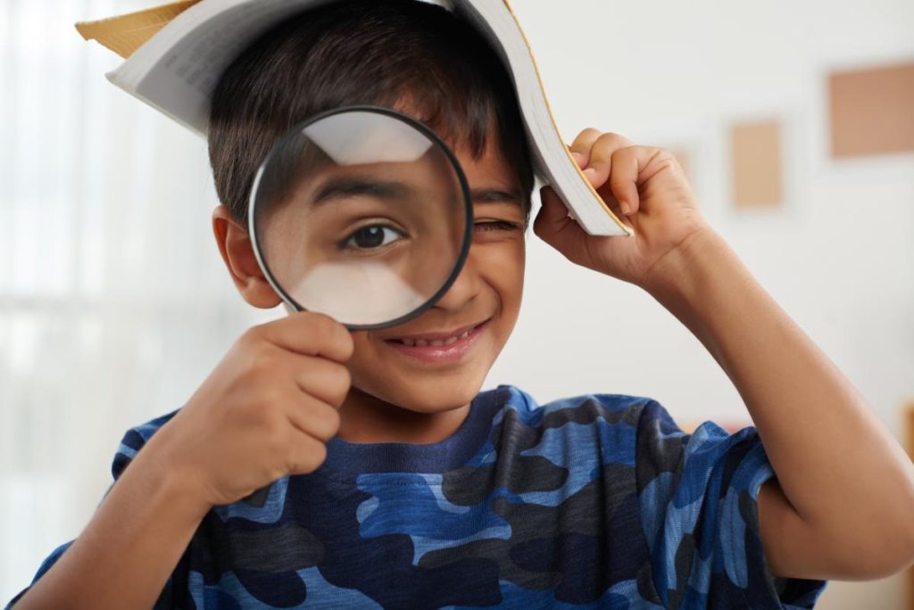 Child looking through magnifying glass with a book on their head