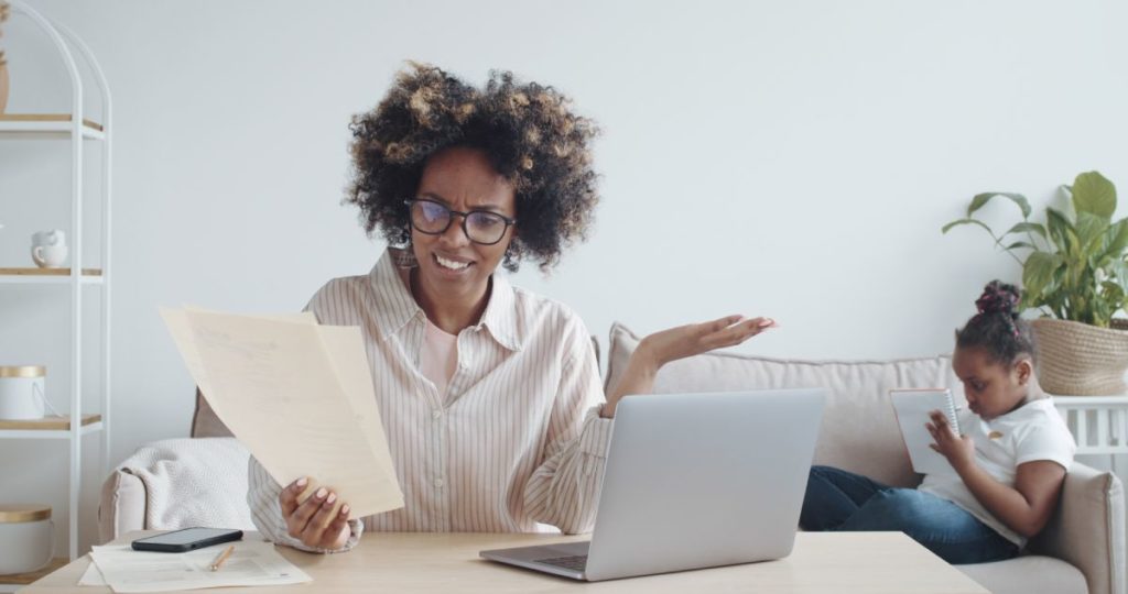 woman with laptop, looking at a piece of paper confused.