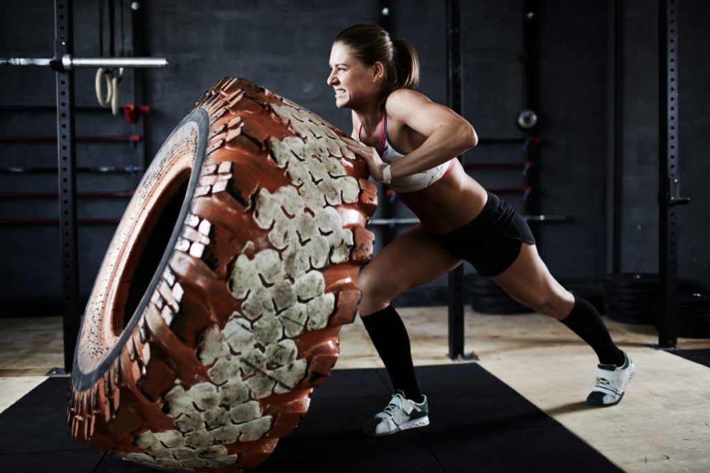 woman exerting effort to push an oversized tire in a gym
