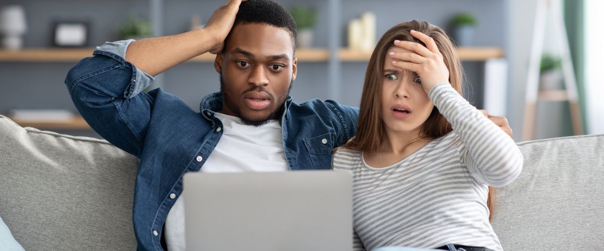 interracial couple looking at a laptop and touching their heads in disbelief