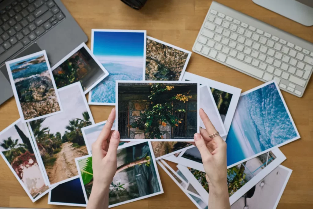 hands holding photos above scattered stack of photos at a desk with multiple keyboards